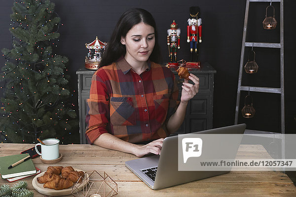 Junge Frau mit Laptop beim Croissantessen zur Weihnachtszeit