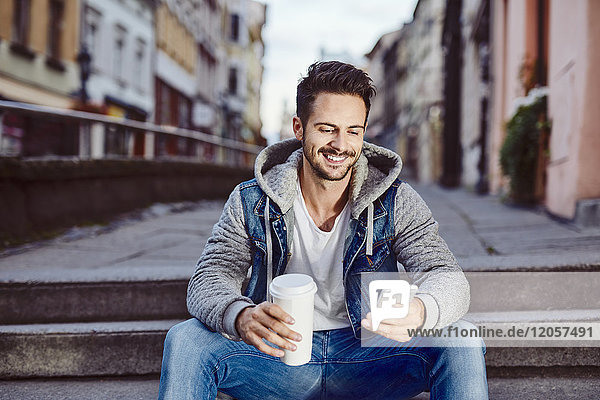 Mann mit Kaffee sitzt auf der Treppe in der Stadt mit dem Telefon