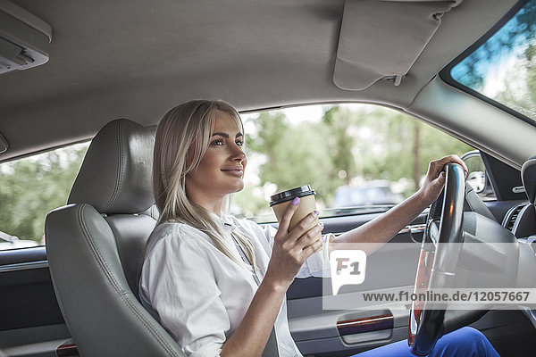 Lächelnde Geschäftsfrau hält Kaffee zum Mitnehmen und fährt Auto