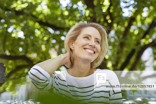 Porträt einer glücklichen blonden Frau vor einem Baum