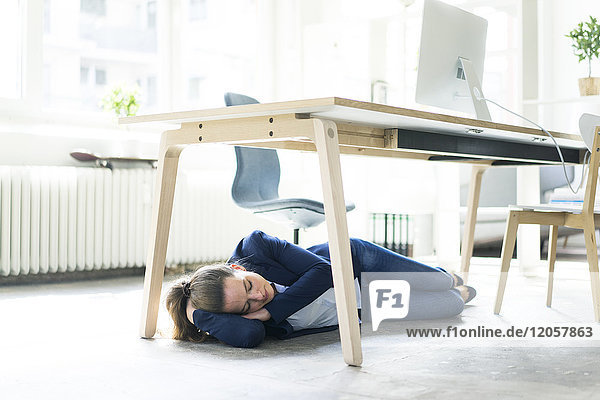 Businesswoman lying under the table in office sleeping