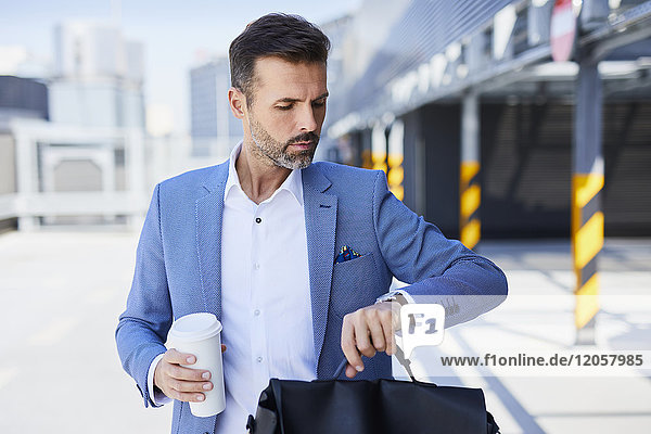 Geschäftsmann kontrolliert die Zeit und hält Kaffee im Freien.