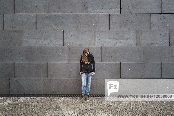 Young woman standing in front of grey facade looking up