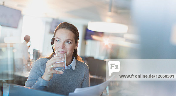 Geschäftsfrau mit Headset trinkt Wasser im Büro