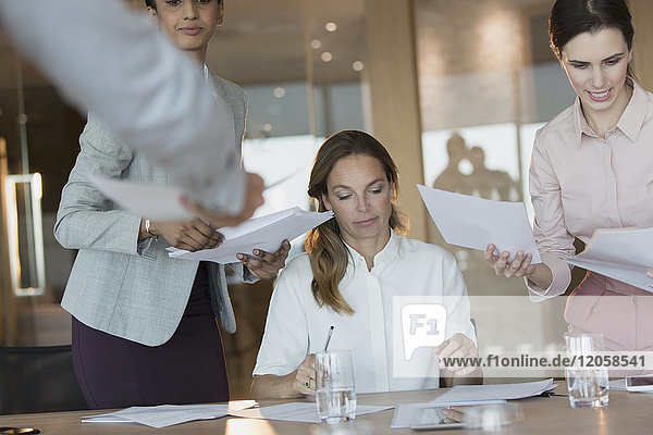 Business people signing and reviewing paperwork in conference room meeting