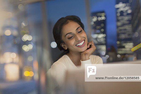 Lächelnde Geschäftsfrau  die nachts im Büro am Laptop arbeitet