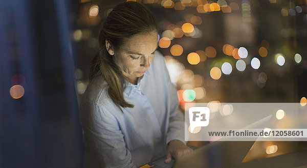 Seriöse  konzentrierte Geschäftsfrau  die nachts am Laptop im Bürofenster arbeitet