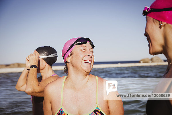 Laughing female open water swimmers talking at sunny ocean