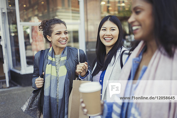 Lächelnde Frauenfreunde mit Einkaufstaschen und Kaffee vor dem Schaufenster