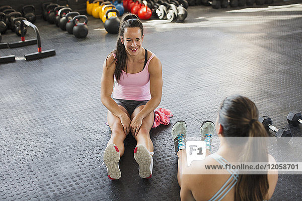 Junge Frauen beim Sprechen und Strecken der Beine im Fitnessstudio
