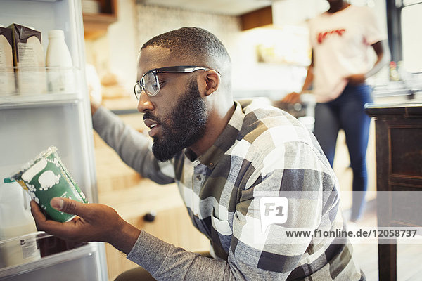 Junger Mann liest Etikett auf Behälter am Kühlschrank