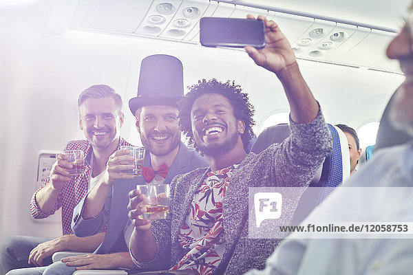 Enthusiastische junge männliche Freunde mit Fotohandy  die trinken und sich selbst im Flugzeug mitnehmen.