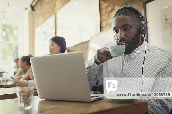 Mann mit Kopfhörer mit Laptop und Kaffeetrinken im Cafe