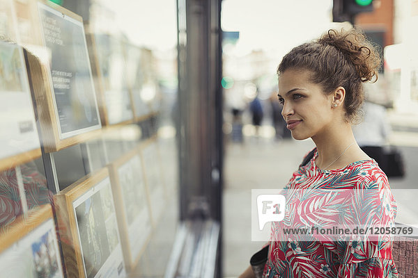 Young woman browsing real estate listings at urban storefront