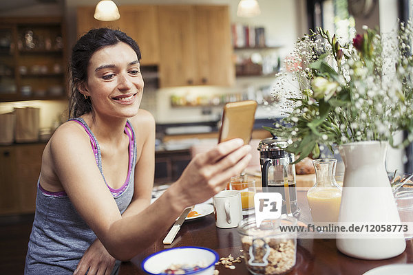 Smiling young woman texting with smart phone at breakfast table