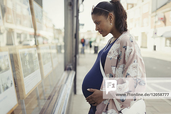Schwangere Frau beim Durchsuchen von Immobilienangeboten im urbanen Schaufenster