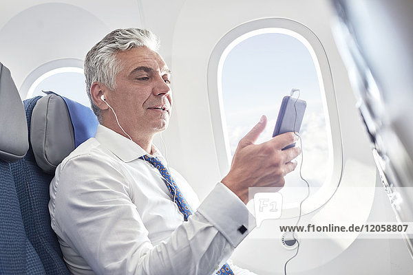 Geschäftsmann beim Musikhören mit Kopfhörer und MP3-Player im Flugzeug