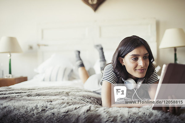 Woman with headphones relaxing on bed  using digital tablet