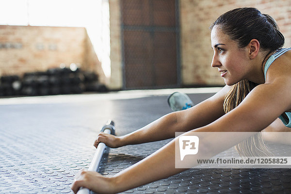 Junge Frau beim Stretching mit Langhantel im Fitnessstudio