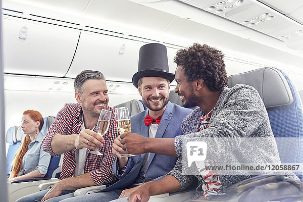 Junge männliche Freunde stoßen in der ersten Klasse im Flugzeug auf Champagnergläser an.