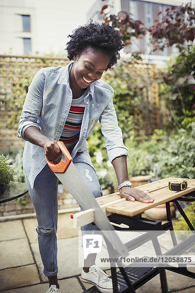 Smiling woman with saw cutting wood on patio