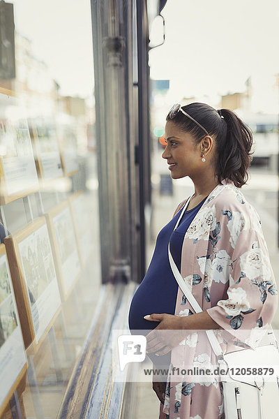 Pregnant woman browsing real estate listings at storefront