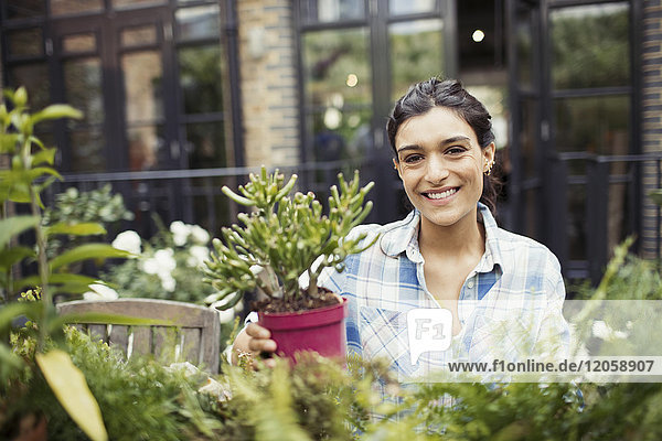 Portrait lächelnde junge Frau im Garten mit Topfpflanzen auf der Terrasse