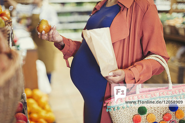 Schwangere Frau beim Einkaufen von Äpfeln im Lebensmittelgeschäft