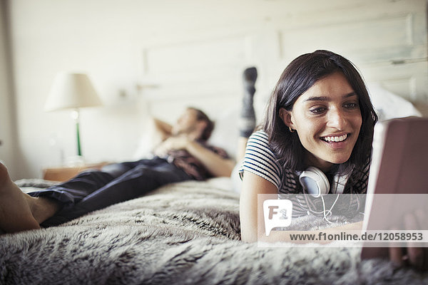Lächelnde junge Frau mit Kopfhörer mit digitalem Tablett auf dem Bett