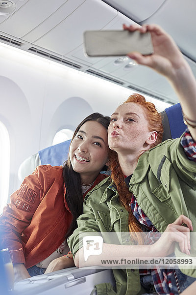 Junge Freundinnen mit Fotohandy posieren für Selfie im Flugzeug