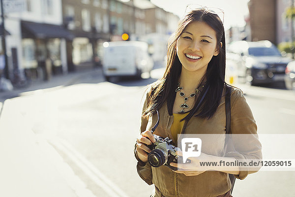 Portrait smiling  confident young female tourist with camera on sunny urban street