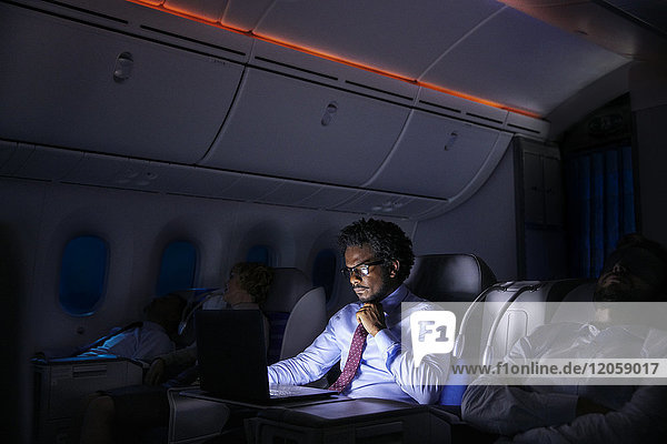 Geschäftsmann bei der Arbeit am Laptop im Nachtflugzeug