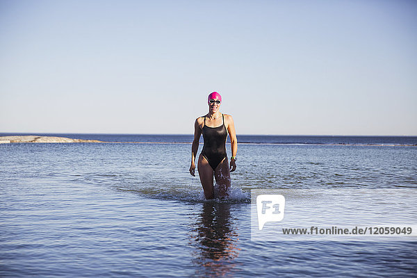 Porträt einer Schwimmerin im offenen Wasser  die im sonnigen Meer spazieren geht.