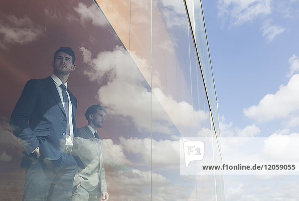Nachdenkliche Geschäftsleute mit Blick aus dem modernen Bürofenster auf sonnigen blauen Himmel und Wolken