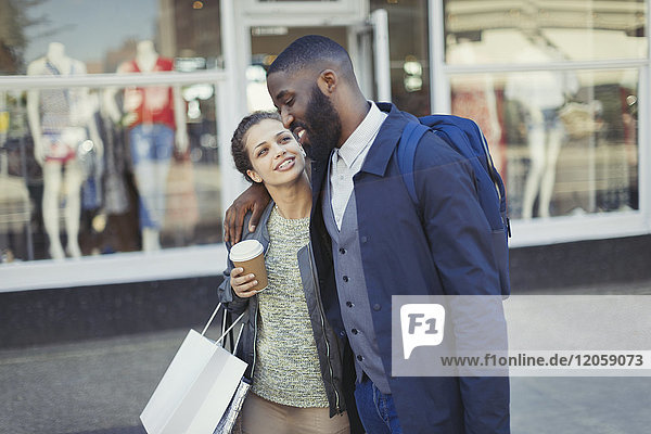 Zärtliches junges Paar mit Kaffee und Einkaufstasche vor dem Schaufenster