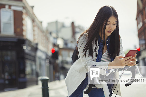Junge Frau pendelt auf dem Fahrrad  SMS mit dem Handy auf der sonnigen Stadtstraße