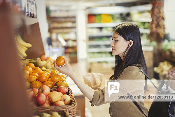 Junge Frau beim Einkaufen  Untersuchung von Orangen im Lebensmittelgeschäft