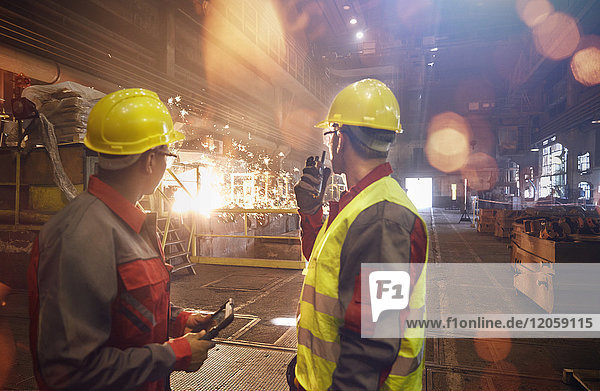Steelworkers with walkie-talkie watching welding in steel mill