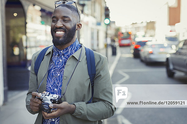 Lächelnder junger männlicher Tourist mit Kamera auf städtischer Straße
