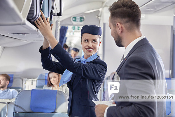 Flight attendant helping businessman with luggage on airplane