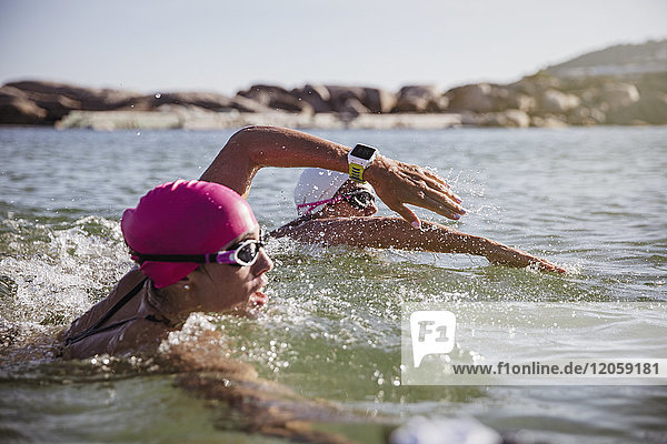 Entschlossene Schwimmerin mit smarter Uhr im sonnigen Meer schwimmend