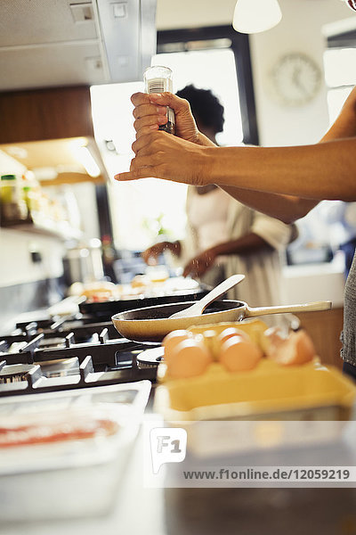 Woman cracking fresh pepper on eggs cooking on stove in kitchen