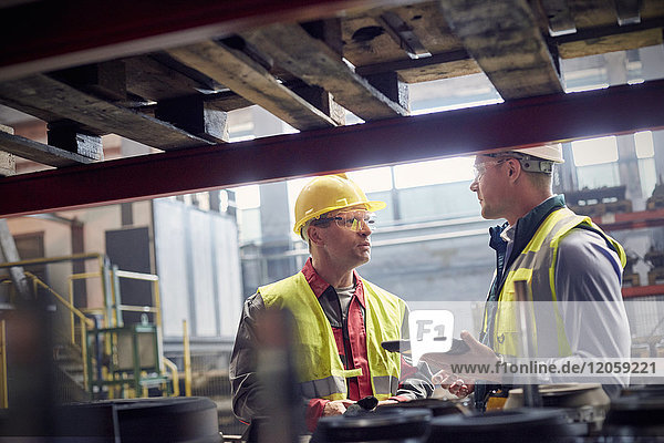 Stahlarbeiter mit digitalem Tablett sprechen im Stahlwerk