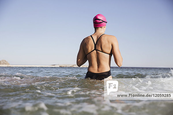 Weibliche Freiwasserschwimmerin beim Waten in der sonnigen Meeresbrandung
