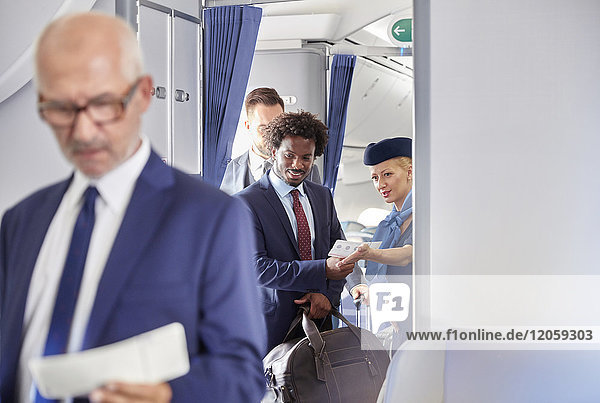 Flugbegleiterin hilft Geschäftsmann mit Bordkarte im Flugzeug