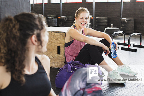 Lächelnde junge Frauen ruhen und trinken Wasser nach dem Training in der Turnhalle