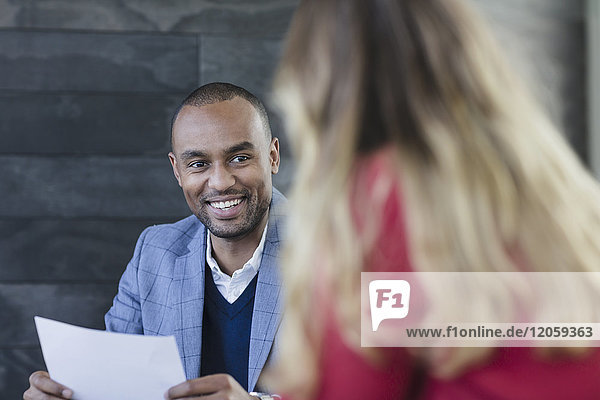 Smiling businessman with paperwork talking with businesswoman in meeting