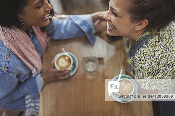 Young affectionate female friends drinking coffee and laughing in cafe