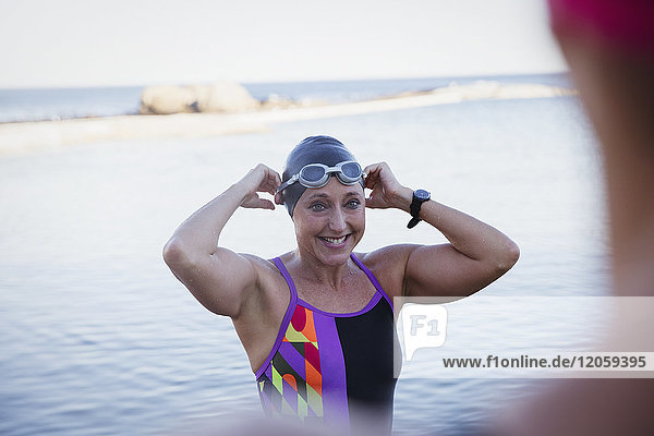 Smiling female open water swimmer adjusting swimming cap and goggles in ocean