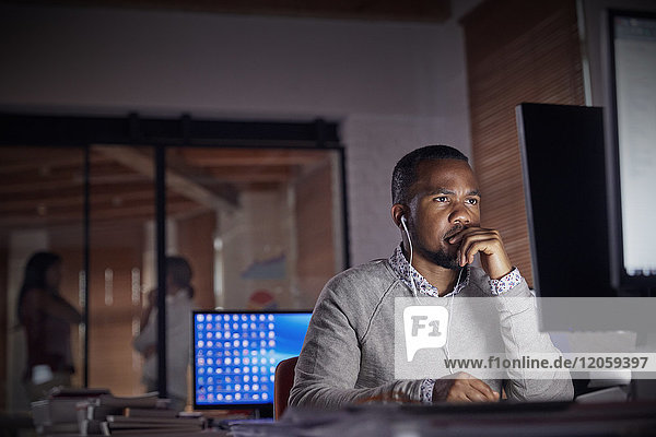 Serious  focused businessman with headphones working late at computer in dark office at night
